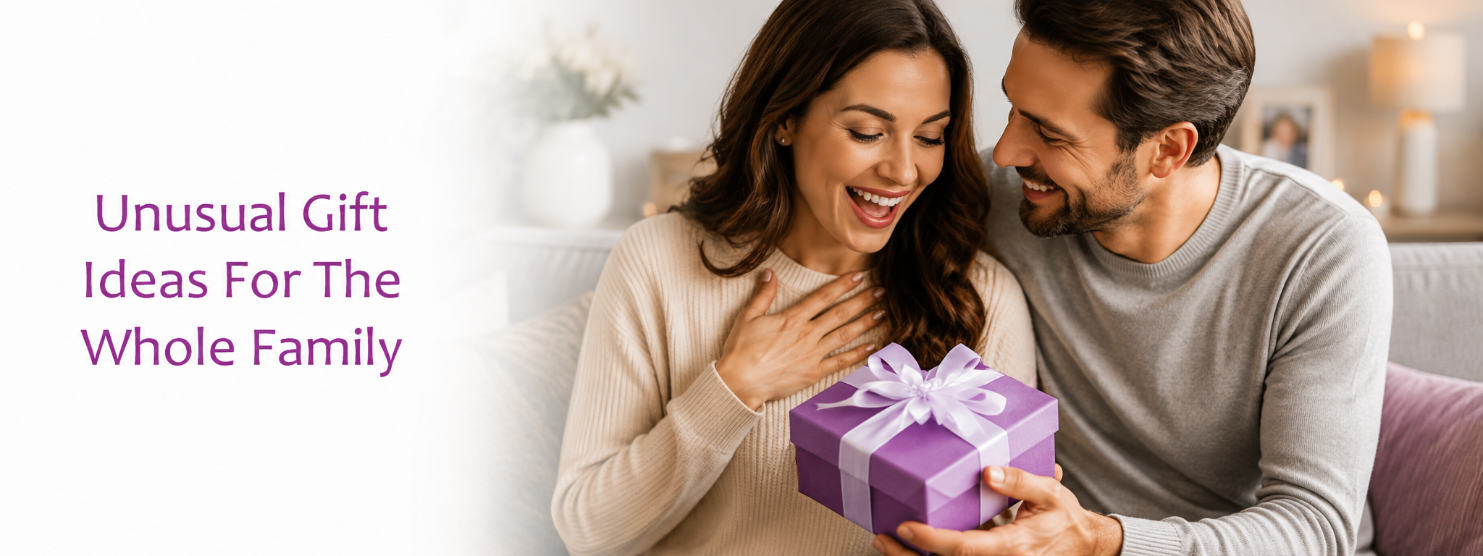 A smiling couple in a cozy living room setting, with the man holding a purple gift box tied with a white ribbon. Text on the left reads 'Unusual Gift Ideas For The Whole Family' in purple.